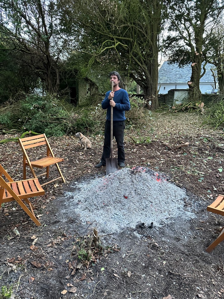 Fiddian standing by the dying embers of the bonfire
