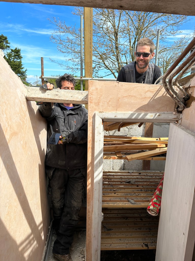Two roof workers looking through a large hole in the roof into a bathroom.