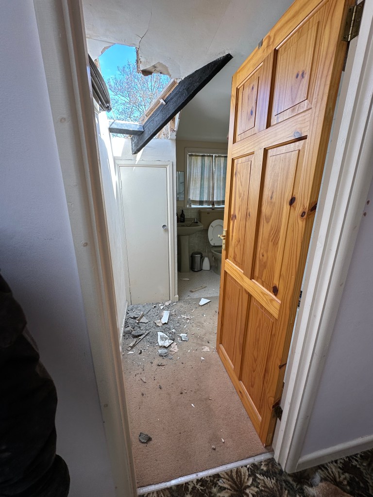 A bathroom with a hole in the roof showing the sky outside.